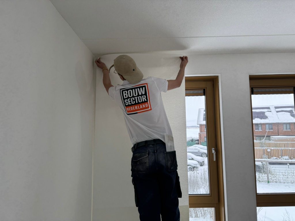 Vakman van Bouwsector Nederland zet een baan behang strak aan tot tegen het plafond