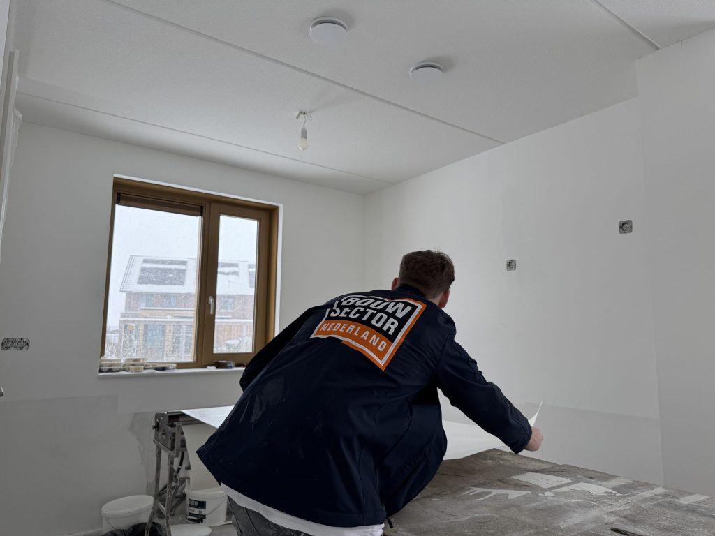 Behanger van Bouwsector Nederland legt een baan behang op de plaktafel in een kale kamer