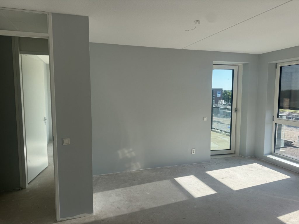 Appartement met egaal gesausde lichtgrijze wanden en een deur naar het balkon