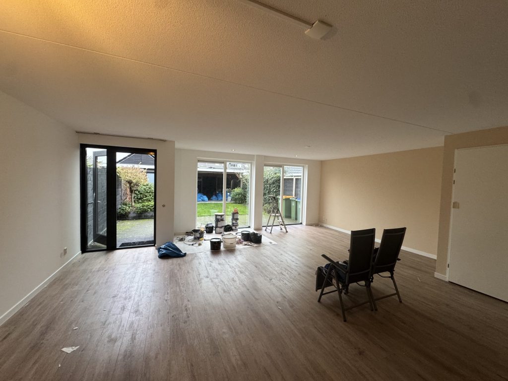 Ruime woonkamer met lichte wanden, een houten vloer en tuindeuren tijdens de afwerking