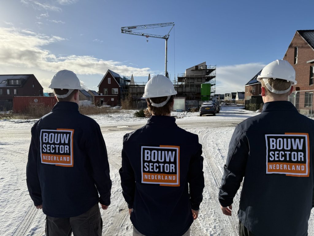 Drie vakmensen van Bouwsector Nederland met witte helm en donkere jas op een besneeuwde bouwplaats