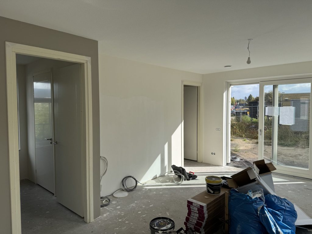 Nieuwbouwwoonkamer met gesausde wanden, tuindeuren en nog materiaal van de afwerking op de vloer